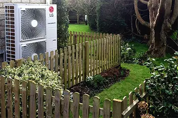 Heat Pumps - a fence and a tree in a yard with a large air con unit