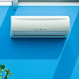 Wall-mounted air conditioner on a bright blue wall, with sunlight casting shadows