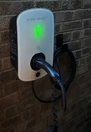 Wall-mounted electric vehicle charger on a brick wall with a glowing green light