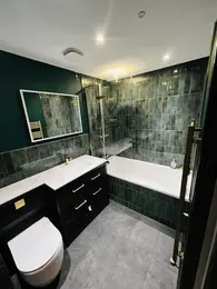 stylish completed bathroom with bathtub and rainfall shower, dark green tiles and fitted vanity unit
