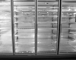 An empty refrigerator display unit in a supermarket, with clear glass doors and shelving