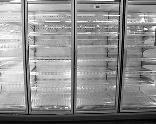 An empty refrigerator display unit in a supermarket, with clear glass doors and shelving