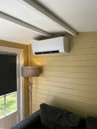 White air conditioner mounted on a yellow wall above a couch and lamp next to a door with a window.