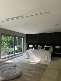 Modern bedroom with large windows, dark headboard, white bedding, and dog beds.