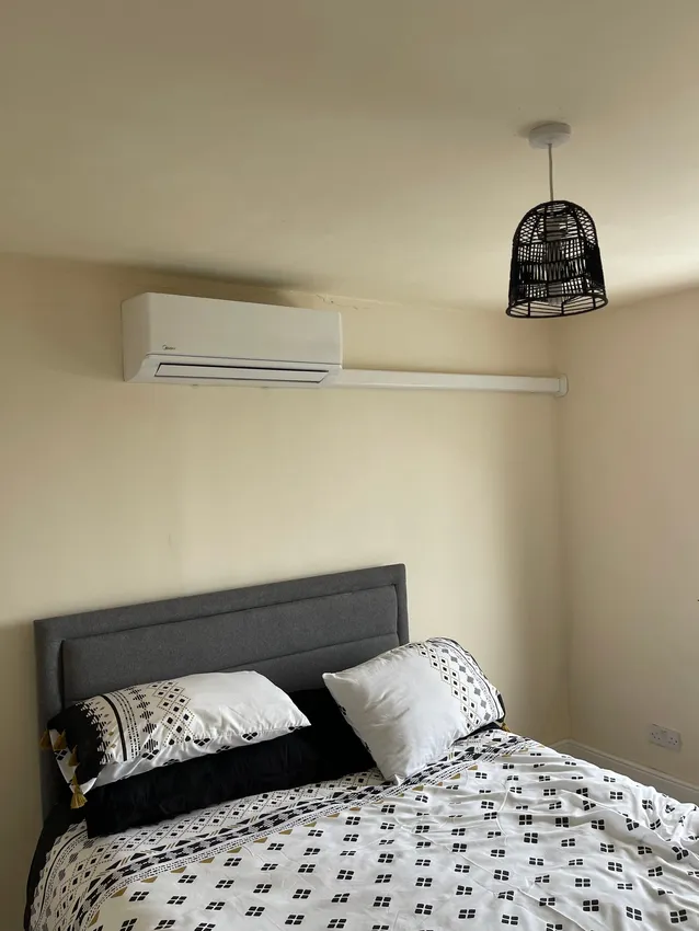 A discreet wall-mounted split air conditioning unit in a modern bedroom