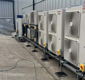 Row of outdoor industrial HVAC units beside a metal building, with vents and control panels on gravel.
